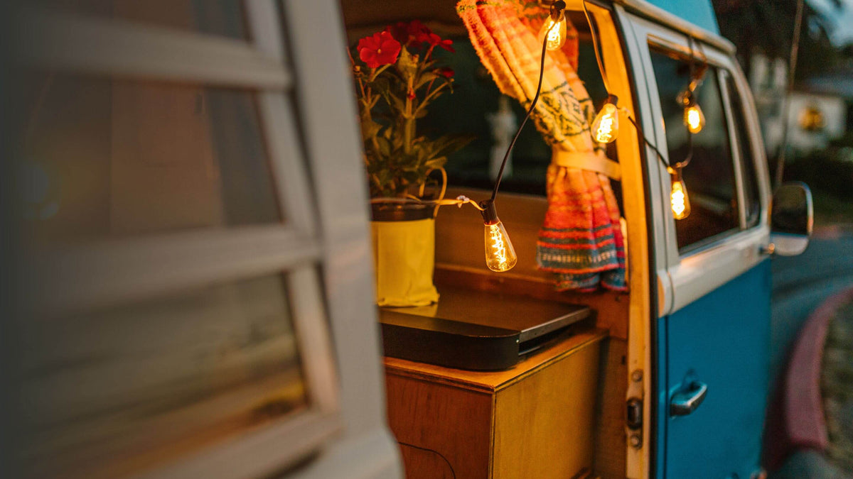 Van aménagé avec porte latérale ouverte, rideau de cabine et guirlande lumineuse au crépuscule