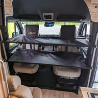Twin removable bunk beds installed above cab seats in a camper van. / Lits superposés amovibles installés au-dessus des sièges avant dans une fourgonnette aménagée.